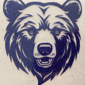May include: A blue glitter bear face design. The bear's head is centered, with detailed features including eyes, nose, and mouth. The glitter adds a sparkling effect to the design, creating a visually appealing image.