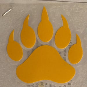 May include: A yellow bear paw print decal. The paw print is outlined in black and has five toes.