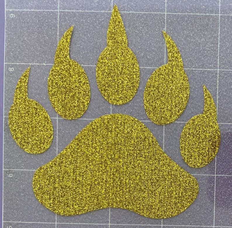 May include: A gold glitter bear paw print with five toes. The paw print is on a gray background.