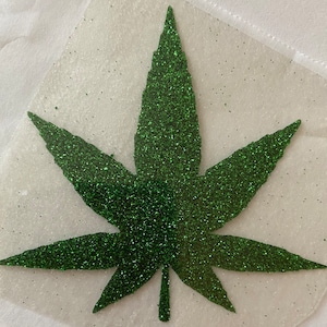 May include: A green glitter cannabis leaf design on a clear background. The leaf has five points and is covered in sparkling green glitter. The design is likely for crafting or apparel.
