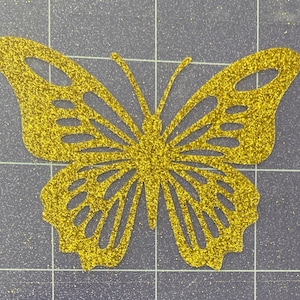 May include: A gold glitter butterfly cutout. The butterfly has a detailed design with intricate wings.