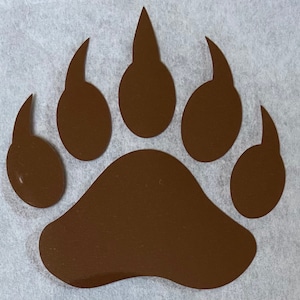 May include: A brown bear paw print decal. The paw print is a silhouette of a bear's paw with five toes.