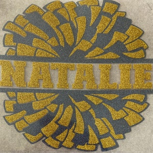 May include: Gold glitter cheerleading pom pom with the name Natalie in gold glitter letters.