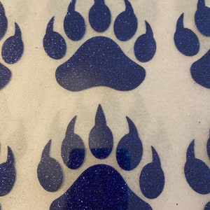May include: Four blue glitter bear paw prints on a white background. The paw prints are in a row, with the top two prints slightly overlapping the bottom two prints.