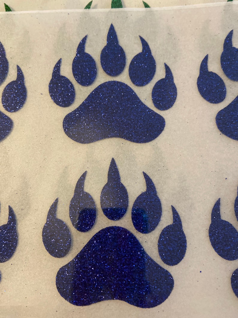 May include: Four blue glitter bear paw prints on a white background. The paw prints are in a row, with the top two prints slightly overlapping the bottom two prints.