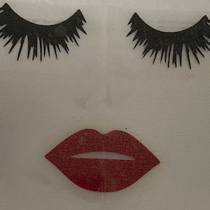 May include: Two black false eyelashes and a red glitter lip sticker on a white background.