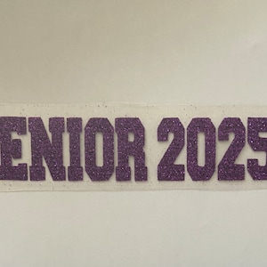 May include: Purple glitter iron-on transfer with the text "Senior 2025".