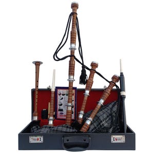 Puede incluir: Un juego completo de gaita en un estuche negro. Las gaitas son de madera y metal, con un cordón y borla negros. El estuche está forrado con tela roja y contiene componentes adicionales. También se ve una tela a cuadros.