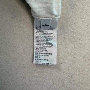 May include: A close-up of a white fabric with a tag attached. The tag has text in multiple languages, including English and French, with washing instructions and a size indicator.