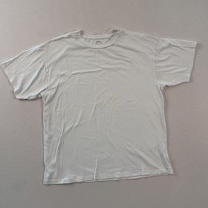 May include: A pale-coloured, short-sleeved t-shirt. The shirt has a crew neck and appears to be made of a soft material. The shirt is laid flat on a neutral surface.