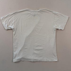 May include: A pale beige short-sleeved t-shirt. The shirt features a crew neck and is made from a soft, lightweight material. The t-shirt is laid flat on a neutral surface.