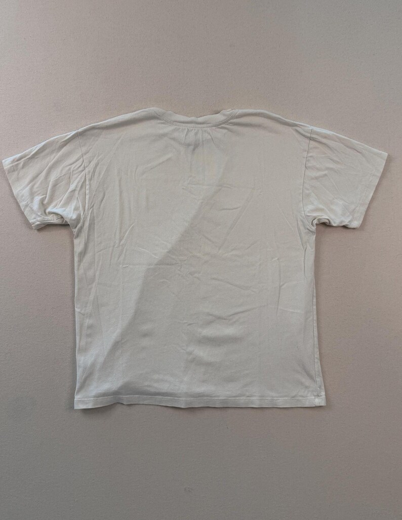 May include: A pale beige short-sleeved t-shirt. The shirt features a crew neck and is made from a soft, lightweight material. The t-shirt is laid flat on a neutral surface.