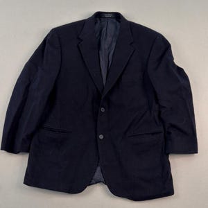 Könnte beinhalten: Ein einfarbiger marineblauer Blazer mit steigendem Revers, zwei Knöpfen auf der Vorderseite und zwei Pattentaschen. Die Jacke ist vollständig mit einem passenden dunklen Innenstoff gefüttert und hat ein kleines Markenetikett am inneren Kragen.
