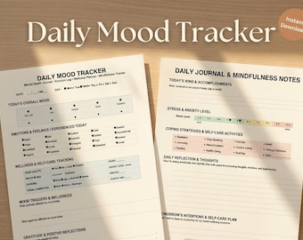 May include: Two printable mood tracker sheets with the text "Daily Mood Tracker" and "Daily Journal & Mindfulness Notes." The sheets include sections for tracking mood, emotions, and self-care activities. A mug of tea and a pen are also visible.