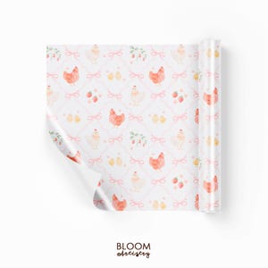 May include: A roll of white wrapping paper with a repeating pattern of chickens, chicks, strawberries, and pink bows. The text "BLOOM Artistry" is at the bottom. The paper is partially unrolled, revealing the pattern.
