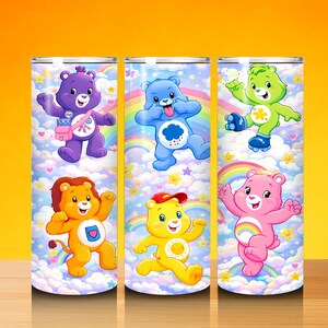 May include: Three stainless steel tumblers with Care Bears designs. Each tumbler displays a different bear character against a backdrop of rainbows, clouds, and stars. The bears are in various poses, adding a playful touch to the drinkware.