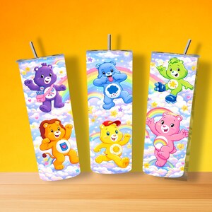 May include: Three stainless steel tumblers with Care Bear designs. Each tumbler features a different Care Bear character against a background of rainbows, clouds, and stars. The tumblers have silver lids and straws.