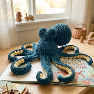 May include: A handmade blue crochet octopus with yellow accents on its tentacles rests on an open book titled "The Tale of Tentacle Tom." The octopus has a round head and eight curled tentacles. The book features colorful illustrations.