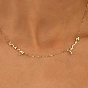 May include: A gold necklace featuring two names, "avery" and "james", in a cursive script. The necklace is worn, highlighting the personalized design. The fine chain adds to the elegant, minimalist style. A delicate piece of jewellery.