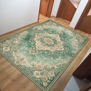 K&ouml;nnte beinhalten: Ein rechteckiger Teppich im Used-Look mit einem zentralen Medaillon-Design. Der Teppich hat eine dominierende tealgr&uuml;ne Farbe mit cremefarbenen und orangefarbenen Blumenmustern. Er liegt auf einem Holzboden und verleiht dem Raum W&auml;rme.