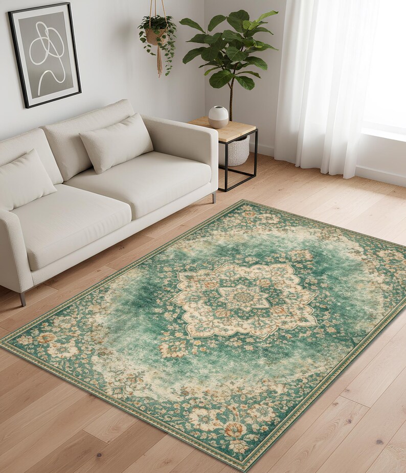 K&ouml;nnte beinhalten: Ein rechteckiger Teppich mit einem Used-Look-Design im Vintage-Stil. Der Teppich hat ein zentrales Medaillonmuster in Creme und Beige, umgeben von einem t&uuml;rkis-gr&uuml;nen Rand mit floralen Motiven. Der Teppich liegt auf einem Holzboden.