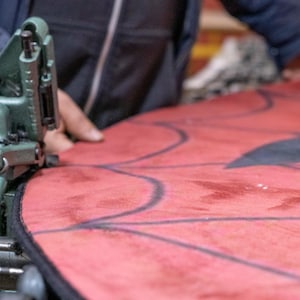 Puede incluir: Primer plano de una tela roja cosida con una m&aacute;quina de coser verde vintage. La tela tiene un dise&ntilde;o de contorno negro. La imagen muestra el proceso de creaci&oacute;n de un art&iacute;culo personalizado.