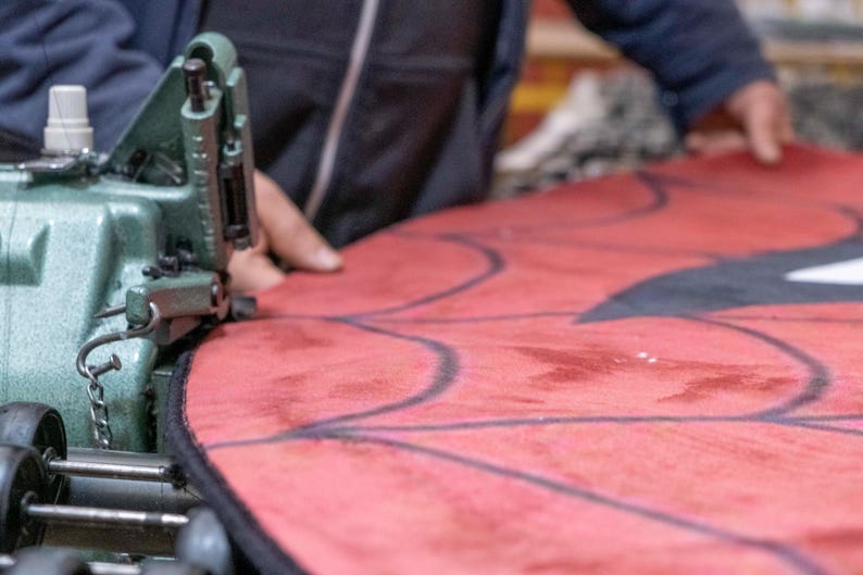 Puede incluir: Primer plano de una tela roja cosida con una m&aacute;quina de coser verde vintage. La tela tiene un dise&ntilde;o de contorno negro. La imagen muestra el proceso de creaci&oacute;n de un art&iacute;culo personalizado.