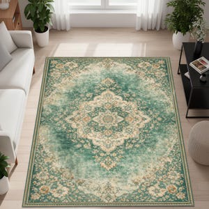 K&ouml;nnte beinhalten: Ein rechteckiger Teppich mit traditionellem Design. Der Teppich hat ein zentrales Medaillon in Creme- und Beiget&ouml;nen, umgeben von einem t&uuml;rkis- und gr&uuml;nen Hintergrund mit floralen Mustern. Der Teppich liegt auf einem hellen Holzboden.