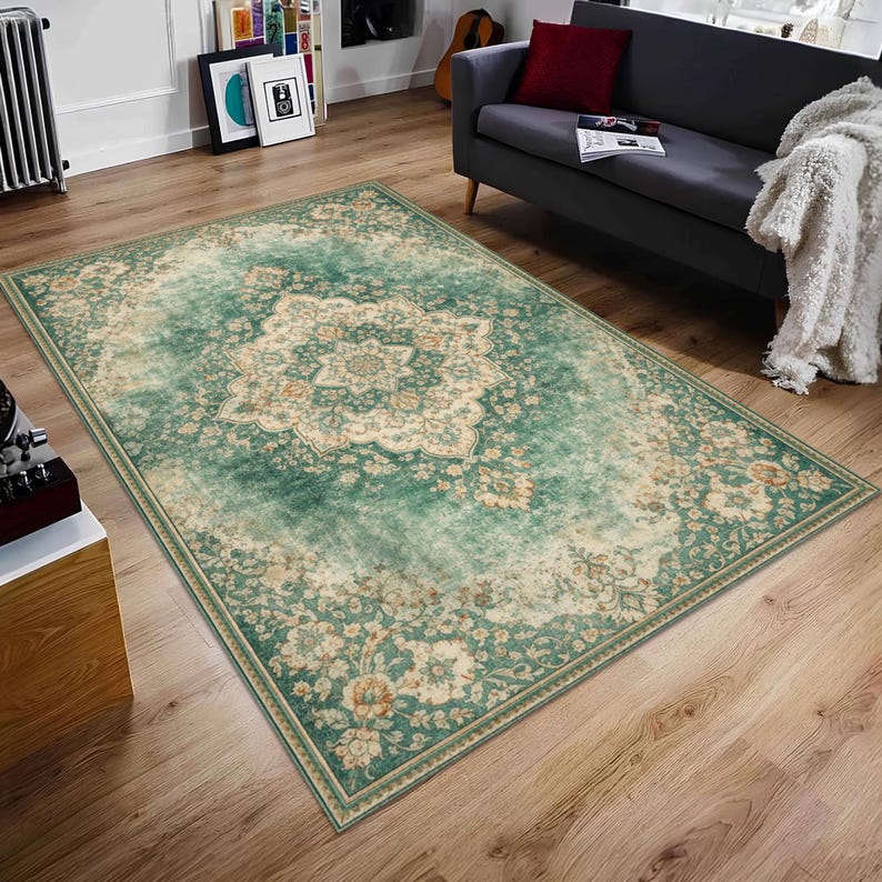 K&ouml;nnte beinhalten: Ein rechteckiger Teppich im Used-Look mit einem zentralen floralen Medaillon-Design. Der Teppich hat eine teal- und beige Farbpalette mit einem detaillierten Rand. Er liegt auf einem Holzboden.