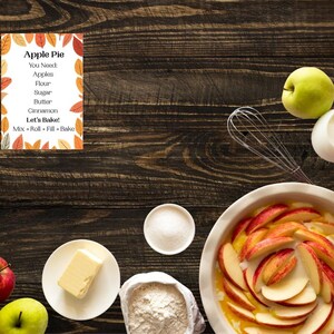 Peut inclure: Une fiche recette intitulée Apple Pie avec une bordure de feuilles d'automne, entourée d'ingrédients dont des pommes rouges et vertes, du beurre, un bol de sucre, un sac de farine, un fouet, un pichet de lait et un plat rempli de pommes tranchées.