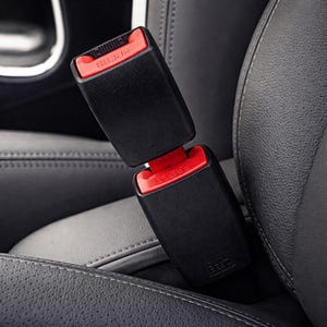 Puede incluir: Primer plano de una hebilla de cinturón de seguridad de coche negra con un botón de liberación rojo. La palabra "PRESS" es visible en el botón. La hebilla está conectada a otra hebilla negra, sobre un asiento de coche de cuero gris oscuro.