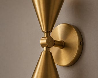 以下が含まれることがあります： ブラッシュドブラス仕上げの壁掛け照明器具で、砂時計のように垂直に配置された2つの円錐形のシェードが特徴です。この照明器具には、円形の取り付けプレートと、2つの円錐をつなぐ中央のジョイントが含まれています。