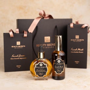 May include: A round glass bottle of Beauty Secrets Skincare Facial Serum No. 1 with a dropper, a tall glass bottle of Facial Mist No. 1, and three black gift bags with pink ribbons, all featuring the brand logo and product text in gold.