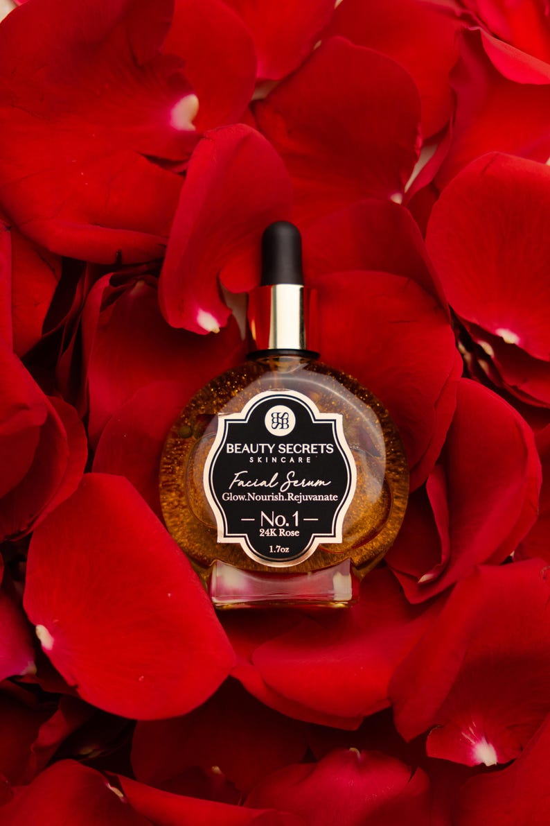 Puede incluir: Un frasco de vidrio redondo de suero facial Beauty Secrets Skincare con tapa de gotero negra. La etiqueta dice Beauty Secrets Skincare, Facial Serum, Glow.Nourish.Rejuvenate, No.1, 24K Rose, 1.7oz. El suero interior es de tono dorado y transl&uacute;cido.
