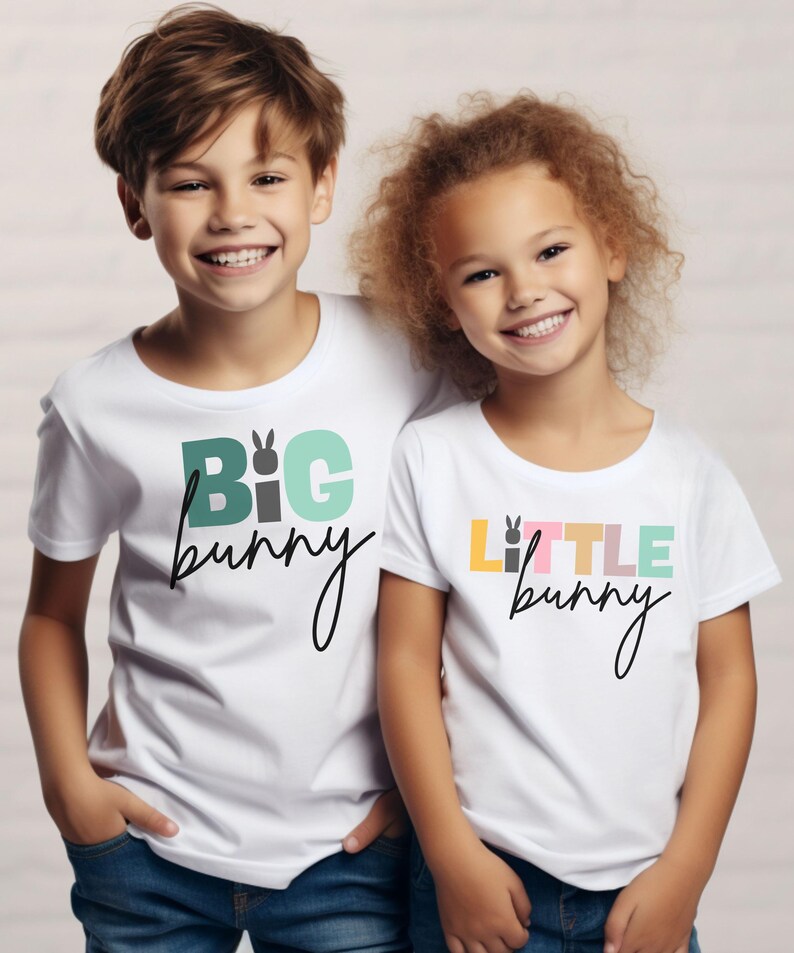 May include: Two children wearing white t-shirts with Easter-themed designs. One shirt says "BIG bunny" in green, gray, and light blue, and the other says "LITTLE bunny" in yellow, pink, and light green. Both shirts have a bunny graphic.
