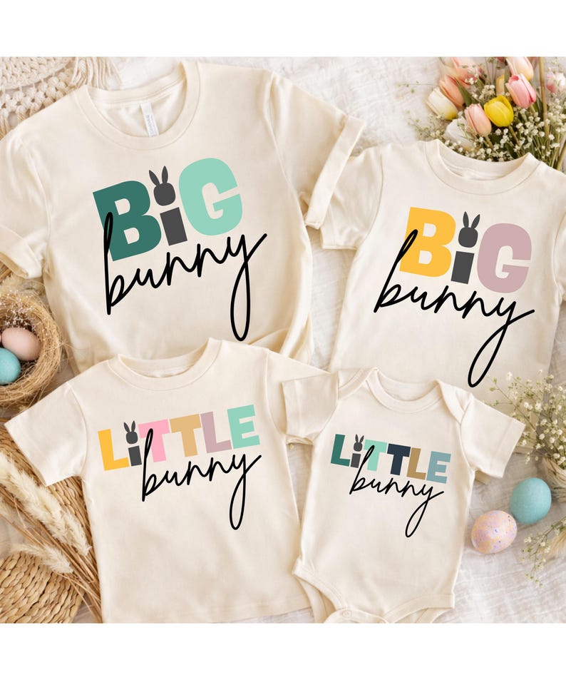 May include: Four cream-colored t-shirts and a onesie with Easter-themed text. The shirts and onesie feature the words "BIG bunny" and "LITTLE bunny" in colorful block letters and a bunny graphic. The text is in black script.