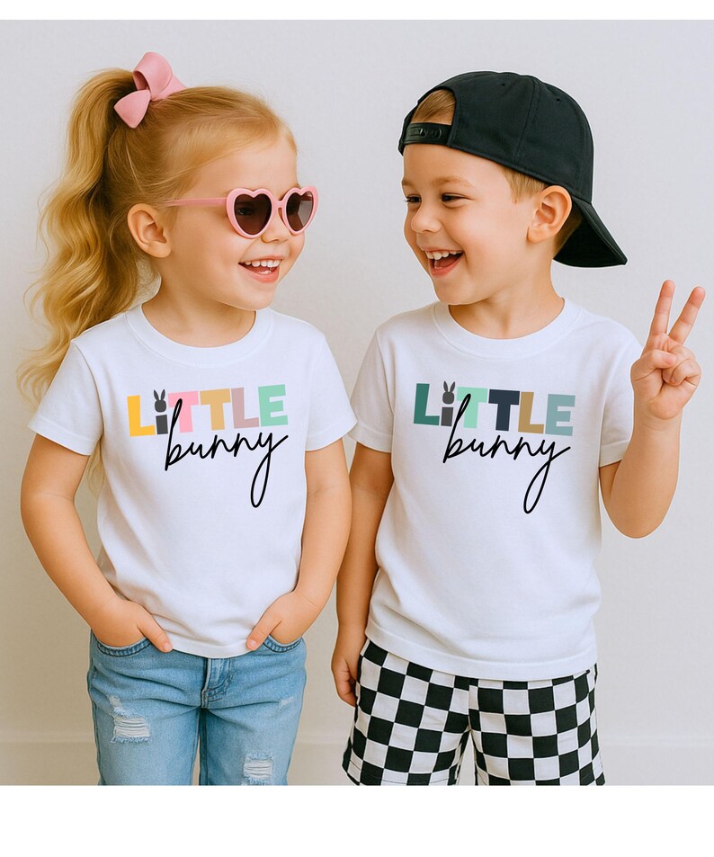 May include: Two children wearing white t-shirts with the text "Little Bunny" in colorful letters. One child wears heart-shaped sunglasses and a pink bow. The other child wears a black baseball cap and checkered shorts.