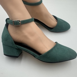 Op de afbeelding: Groene su&egrave;de enkellaarsjes met blokhak en spitse neus. De schoenen hebben een gespsluiting op de enkelband en een lage hak. De schoenen zijn effen donkergroen.