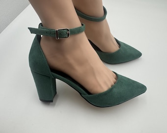 May include: Green suede heels with pointed toes and ankle straps. The shoes have a block heel and a buckle closure. The heels are approximately 3 inches high.