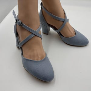 May include: Light blue suede-like heels with crisscross straps and ankle buckles. The shoes have a rounded toe and a block heel. The heels are approximately 3 inches high.