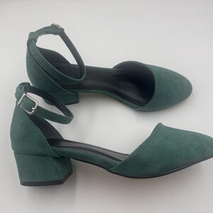 Op de afbeelding: Een paar groene su&egrave;de enkellaarsjes met enkelbandjes. De schoenen hebben een ronde neus, een kleine blokhak en een gespsluiting. De hakken zijn ongeveer 5 cm hoog.