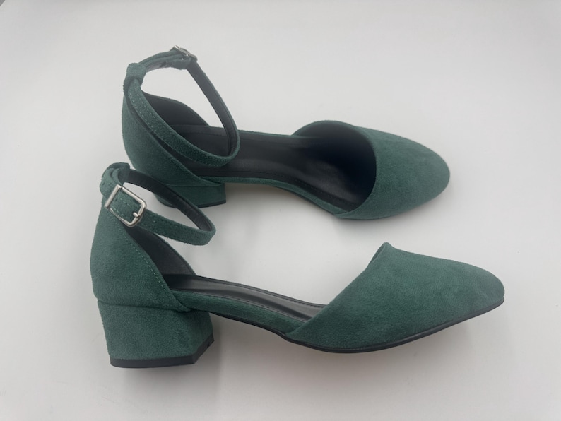 Op de afbeelding: Een paar groene su&egrave;de enkellaarsjes met enkelbandjes. De schoenen hebben een ronde neus, een kleine blokhak en een gespsluiting. De hakken zijn ongeveer 5 cm hoog.