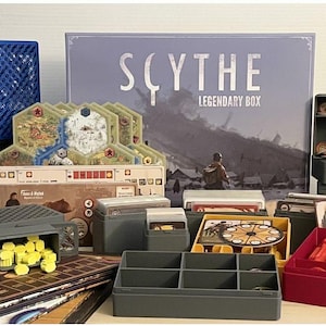 May include: A selection of 3D-printed game organisers and components for the Scythe Legendary Box board game. Includes various coloured storage boxes, trays, and decorative elements. The game box and game pieces are also visible.