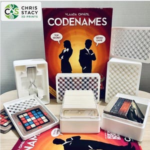 Könnte beinhalten: Brettspiel "Codenames" mit weißen Kunststoffkomponenten, Karten und einem Timer. Die Box zeigt Silhouetten von zwei Figuren und die Wörter "Top Secret" und "Word Game". Das Spiel ist von Vlaada Chvátil.