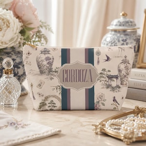 May include: A rectangular zipped pouch featuring a cream-coloured fabric with a toile-style print of blue and purple vases, birds, and floral motifs. A central vertical stripe design contains a decorative label with the name CORDOZA printed.