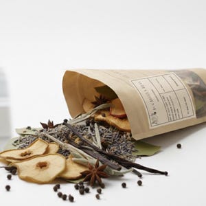 May include: A brown paper bag spilling dried fruit slices, star anise, peppercorns, and other spices onto a white surface. The bag has a label with text. The scene is set in a bright, clean kitchen environment.