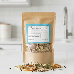 May include: A brown paper bag with a clear window, filled with dried herbs and citrus slices. The bag has a blue label that reads "FRESH & CLEAN" and lists ingredients. Dried rosemary, lemon slices, and peppercorns are scattered around the bag.