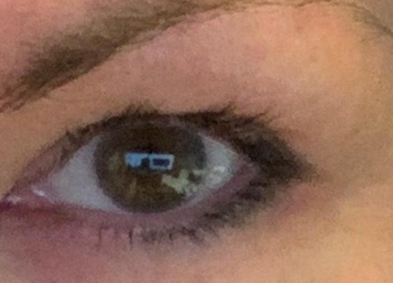 Peut inclure: Gros plan sur un &oelig;il humain avec un iris brun et des cils fonc&eacute;s. L'&oelig;il refl&egrave;te une image floue d'une pi&egrave;ce avec une fen&ecirc;tre et des meubles. La peau autour de l'&oelig;il est brun clair.