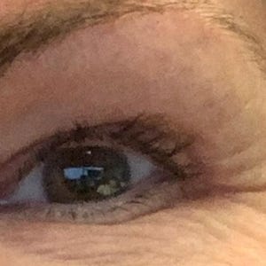 Peut inclure: Gros plan sur un &oelig;il humain avec un iris brun et des cils fonc&eacute;s. L'&oelig;il est partiellement ouvert, r&eacute;v&eacute;lant le reflet d'une fen&ecirc;tre. La peau autour de l'&oelig;il est brun clair avec des rides visibles.