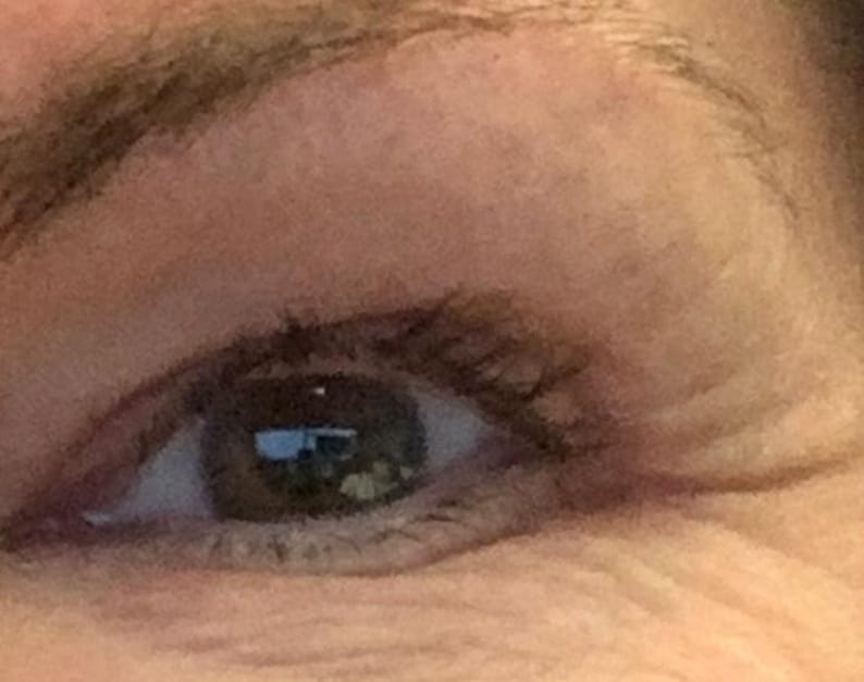 Peut inclure: Gros plan sur un &oelig;il humain avec un iris brun et des cils fonc&eacute;s. L'&oelig;il est partiellement ouvert, r&eacute;v&eacute;lant le reflet d'une fen&ecirc;tre. La peau autour de l'&oelig;il est brun clair avec des rides visibles.